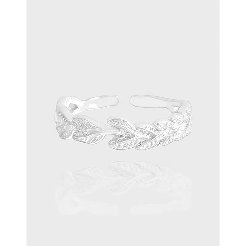 Polished sterling silver open-ring with leaf-engraved motifs on a pale background.
