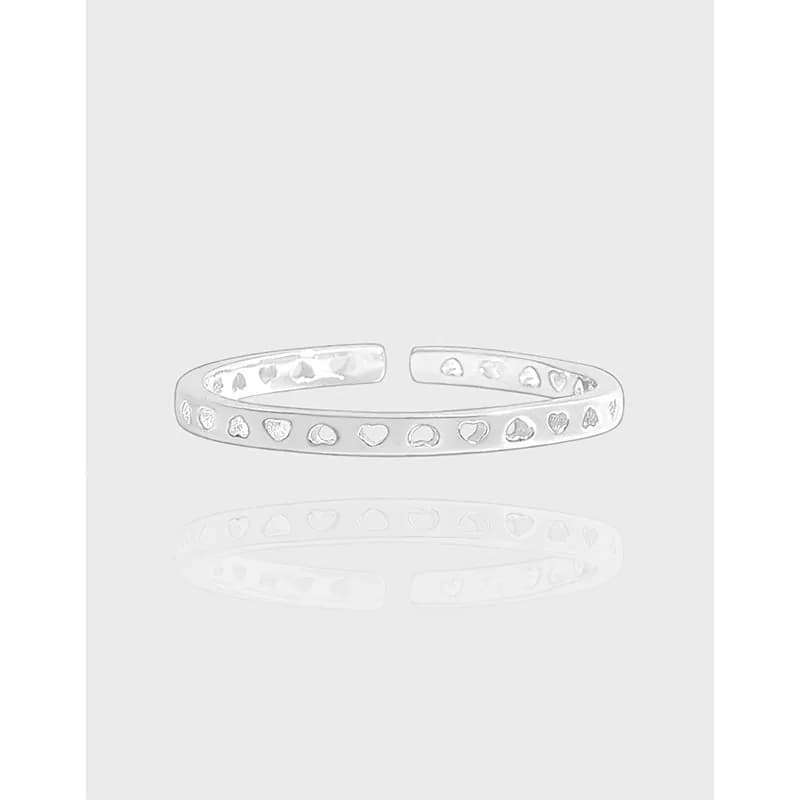 Open sterling silver ring with a row of small heart motifs on a light grey background.