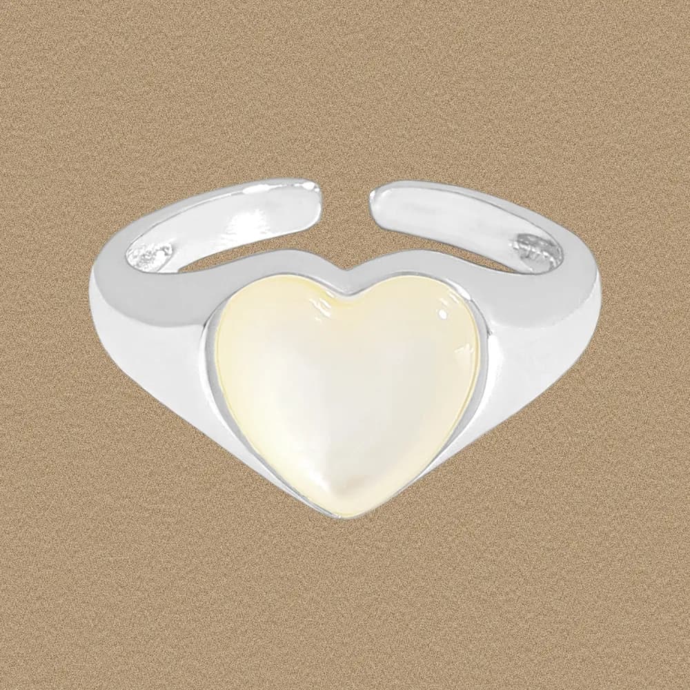Polished sterling silver ring with a pale heart-shaped centerpiece on a beige background.