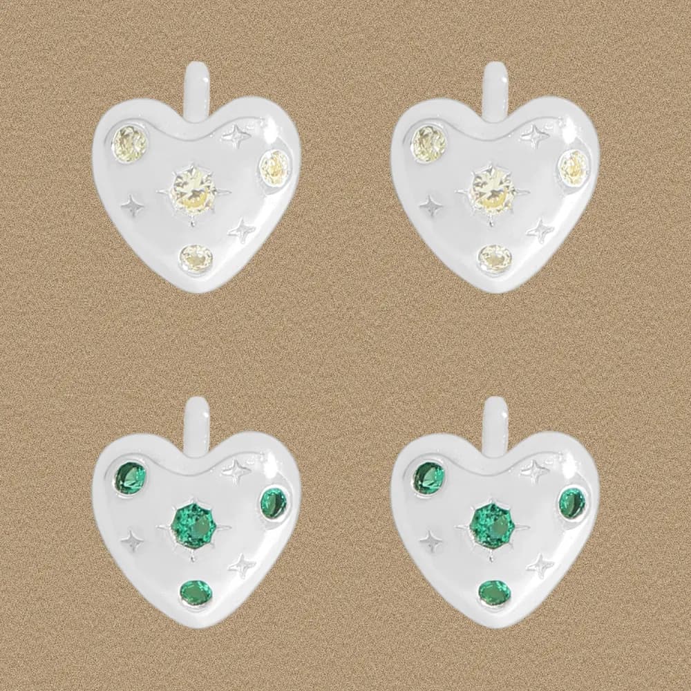 Pair of heart-shaped sterling silver stud earrings with crystal and green stones, shown front-facing on a warm background.
