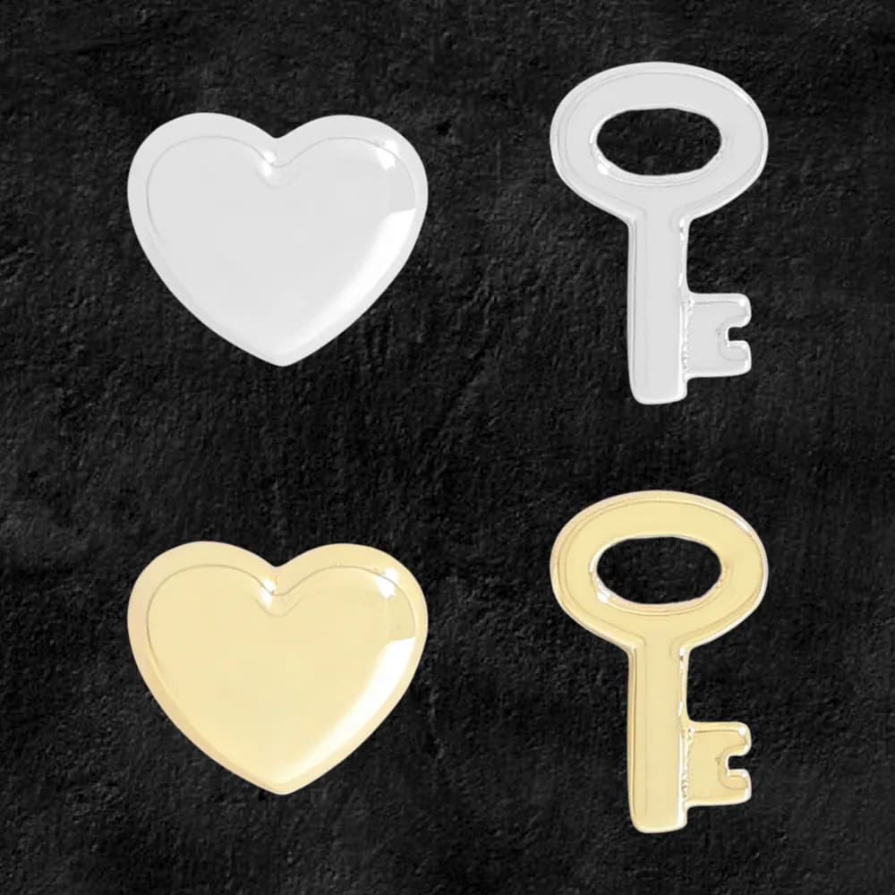Polished heart-shaped stud earrings in silver and gold-tone finishes laid flat on a dark background.