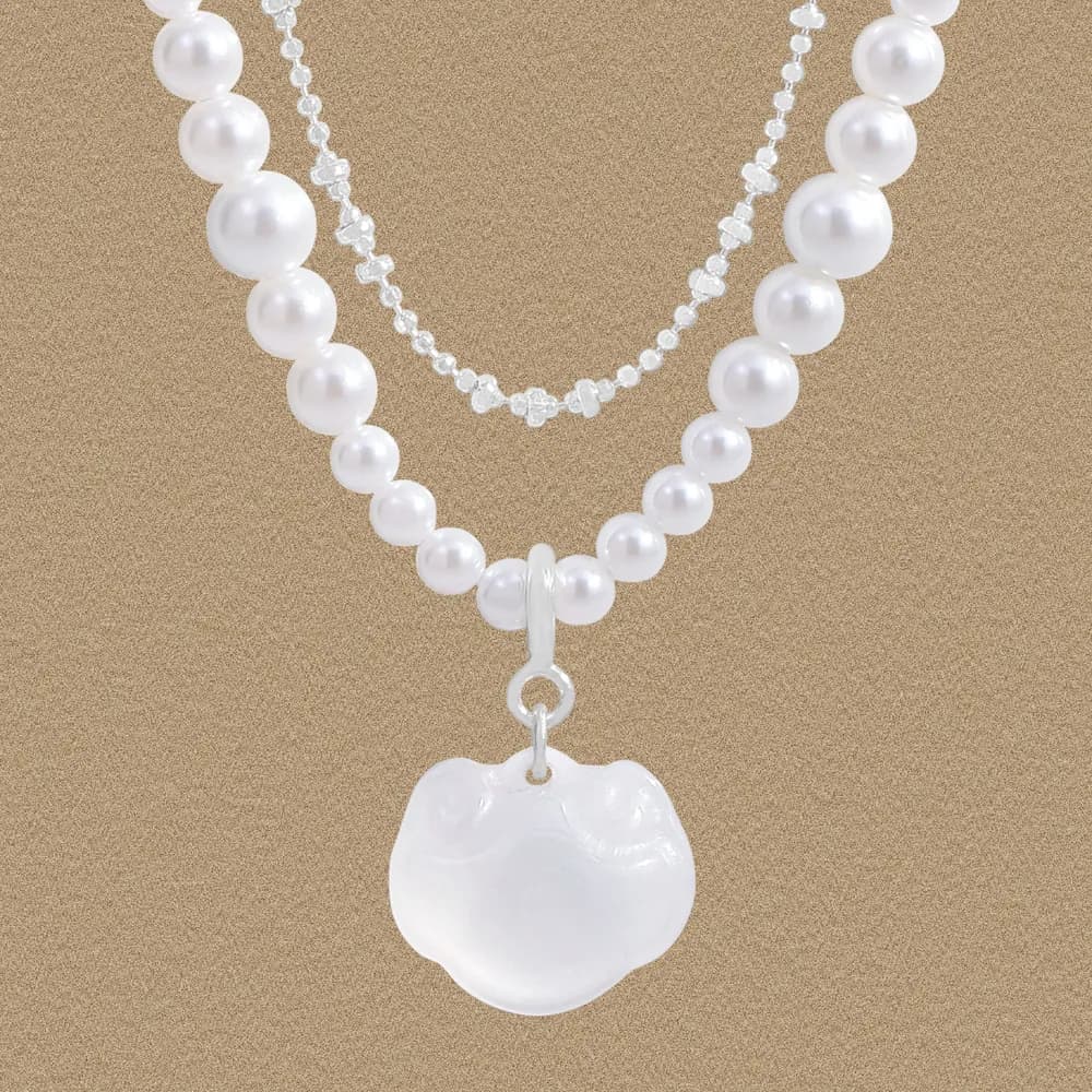 Two pearl necklaces with a heart-shaped pearl pendant hanging against a warm beige background.
