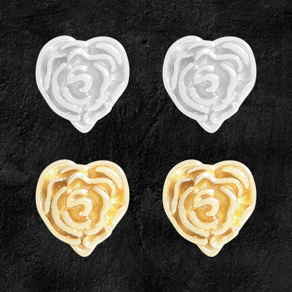 Pair of rose‑pattern heart stud earrings in silver and gold tones on a dark textured background.