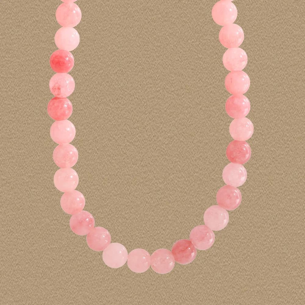 Close-up of a pink rose quartz bead necklace on a warm, sandy background.