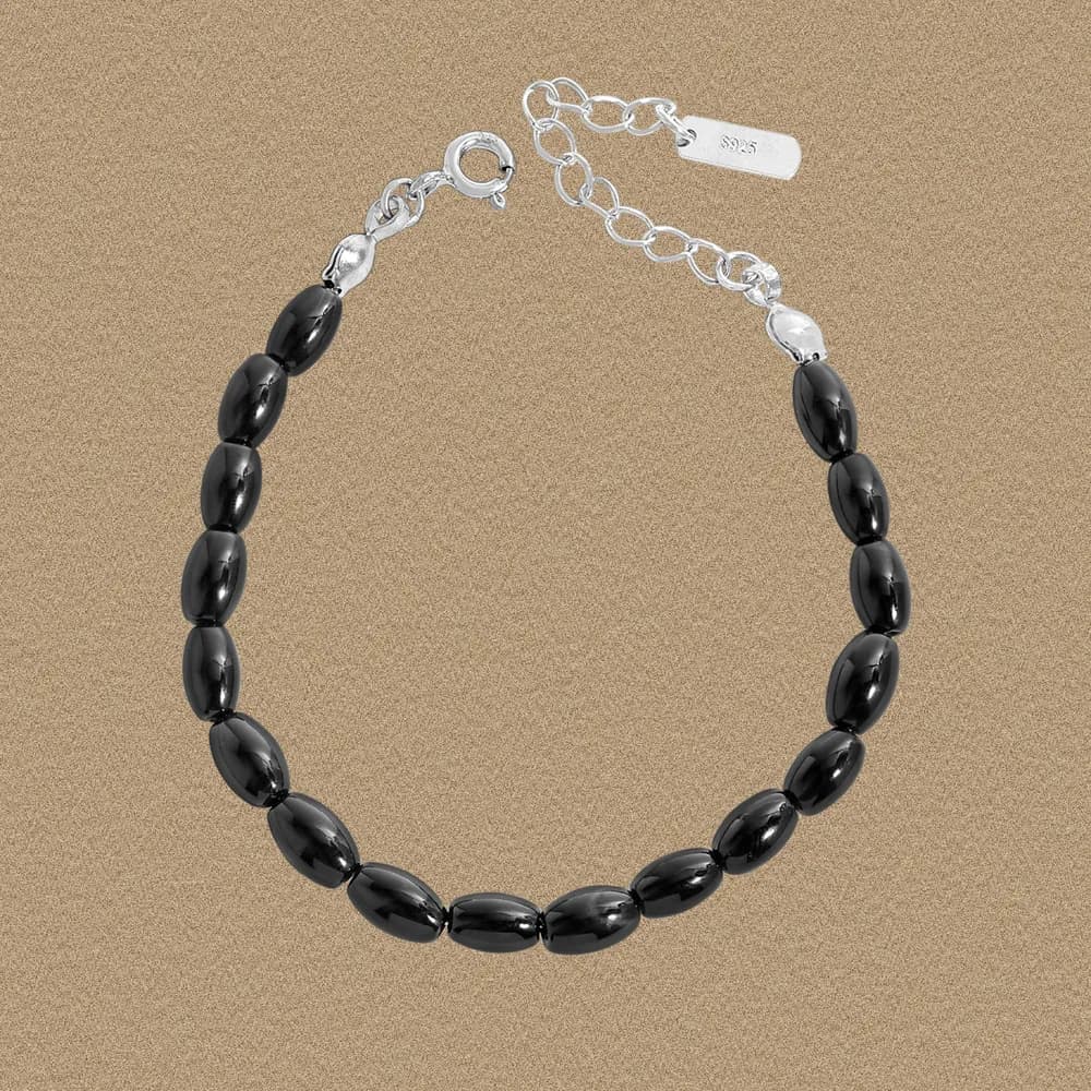 Sterling silver bracelet with glossy black oval beads arranged in a single row and a small extension chain.