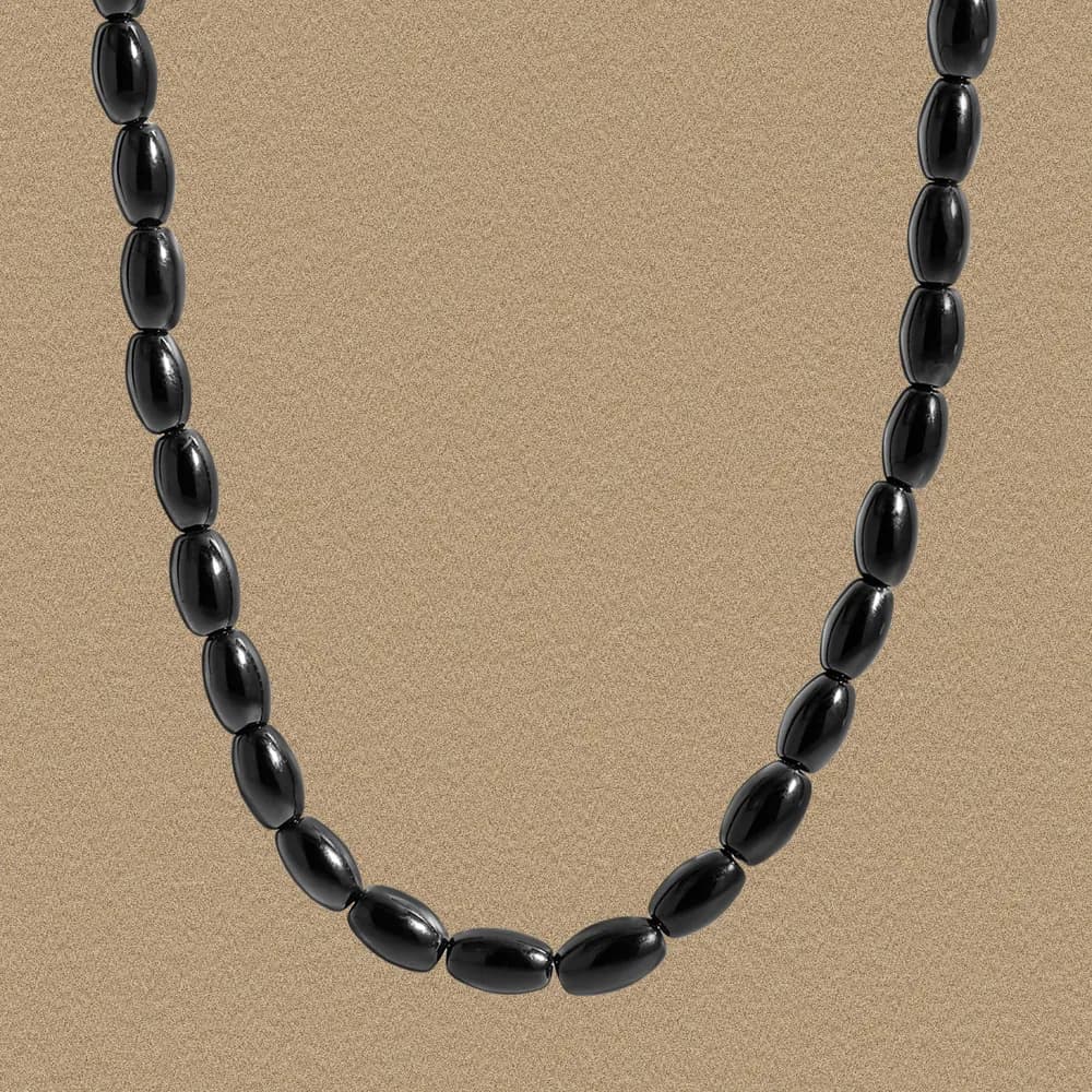 Close-up view of a black oval bead necklace displayed on a beige background.