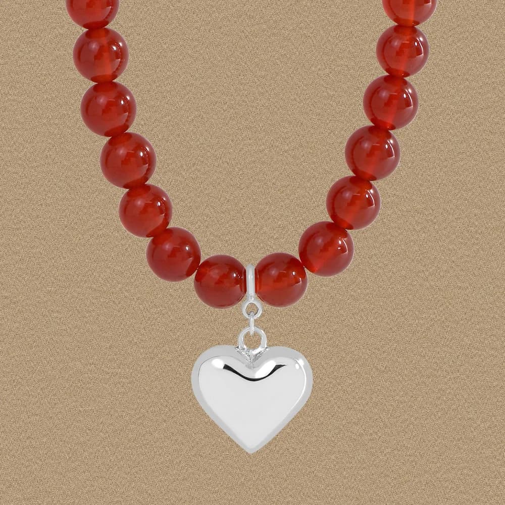 Close-up of a red beaded necklace featuring a silver heart pendant against a neutral backdrop.