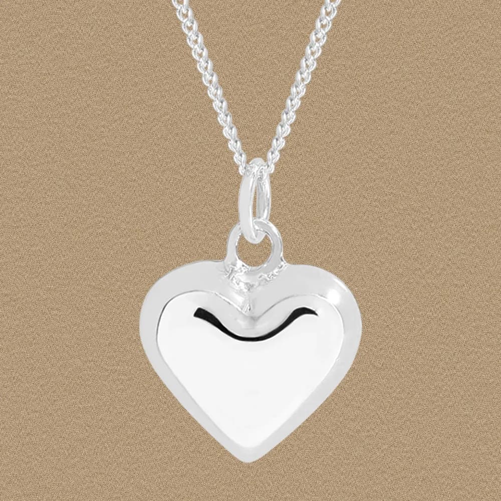 Polished sterling silver heart pendant on a rope chain against a warm beige background.
