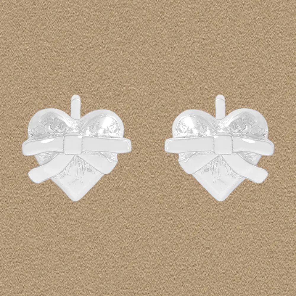 A pair of polished sterling silver heart earrings with a bow across the front, shown on a neutral background.
