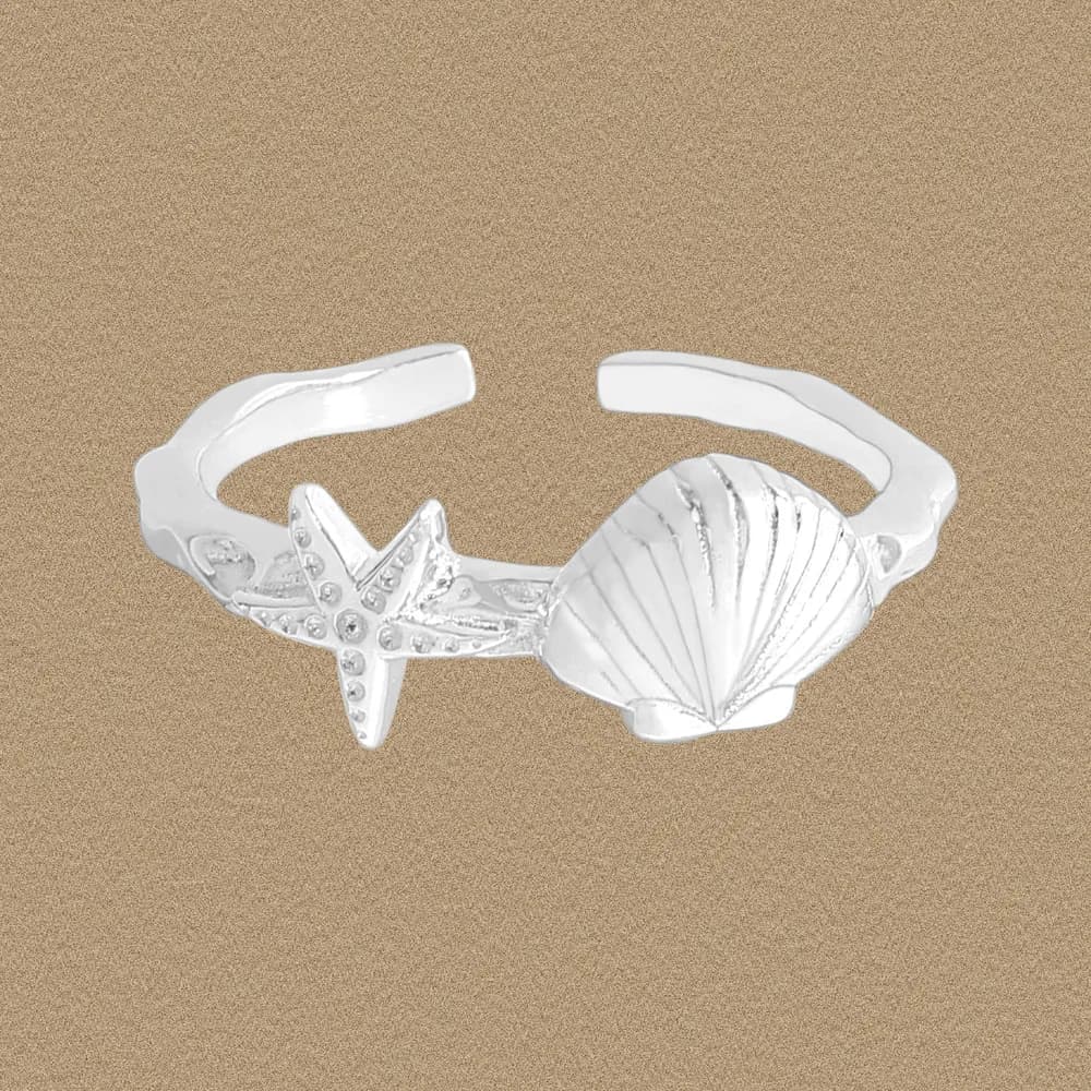 Open polished sterling silver ring with shell and starfish motifs on a sandy background.