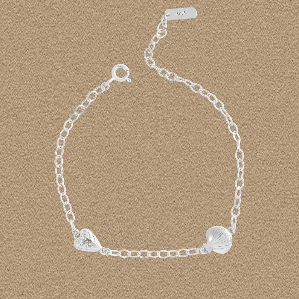 Polished sterling silver bracelet with a seashell charm and a heart cutout charm on a chain