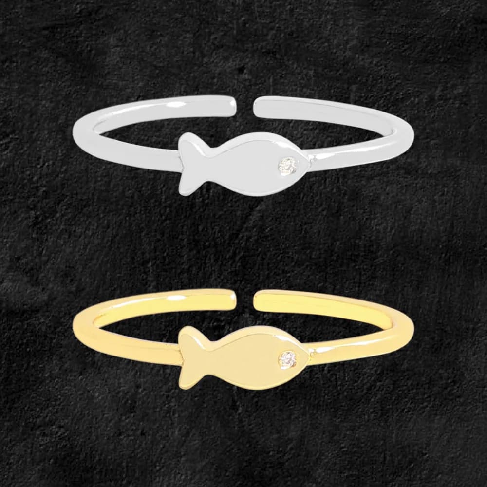 Two polished ring bands with a fish-shaped charm and a small gemstone on the body, shown in silver and gold-tone finishes.