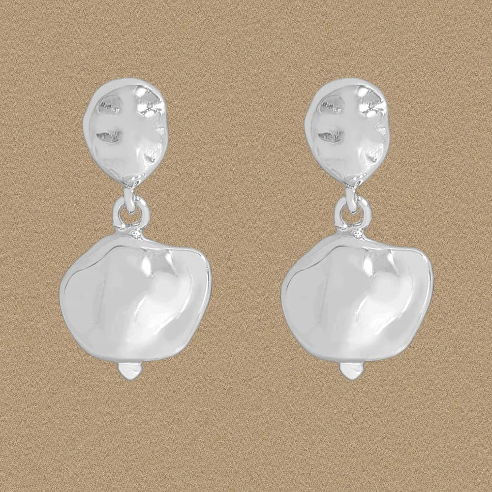Pair of polished sterling silver hammered drop earrings with irregular organic shapes on a warm beige background.