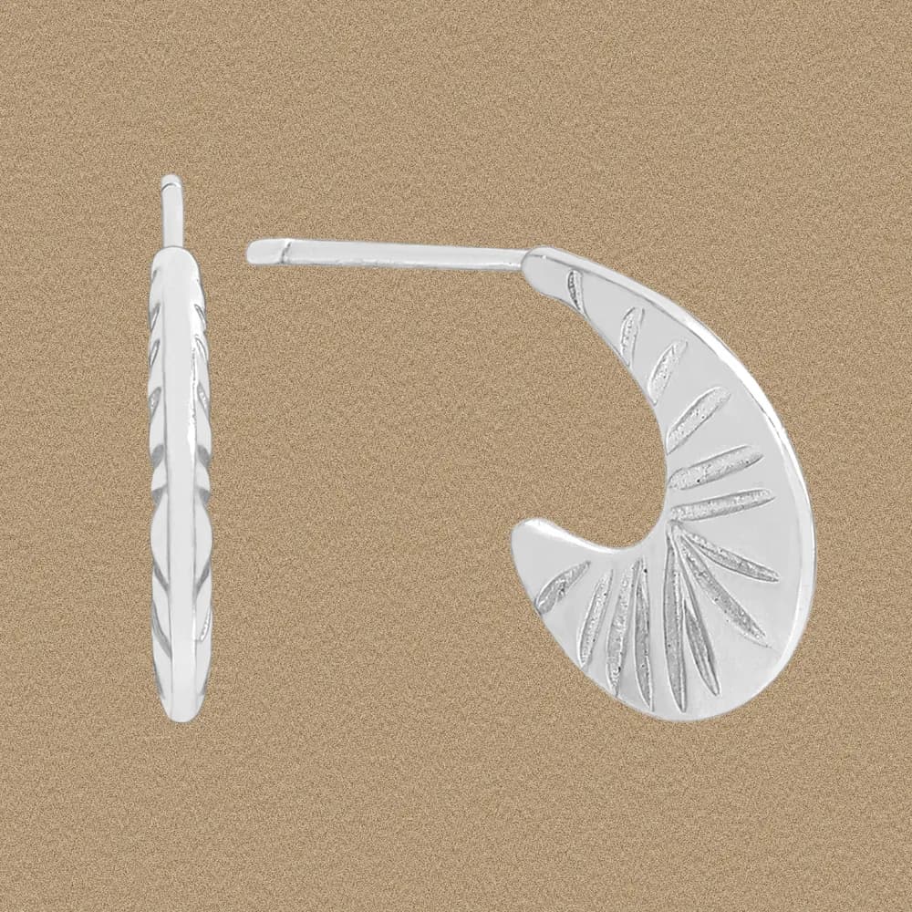 Polished sterling silver crescent-shaped earring with etched sunburst details against a tan background.