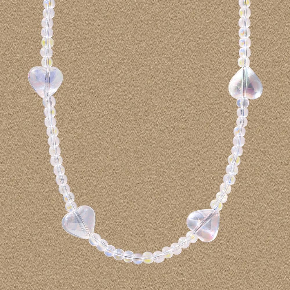 Close-up of a sterling silver beaded necklace with iridescent heart-shaped beads against a sandy background.
