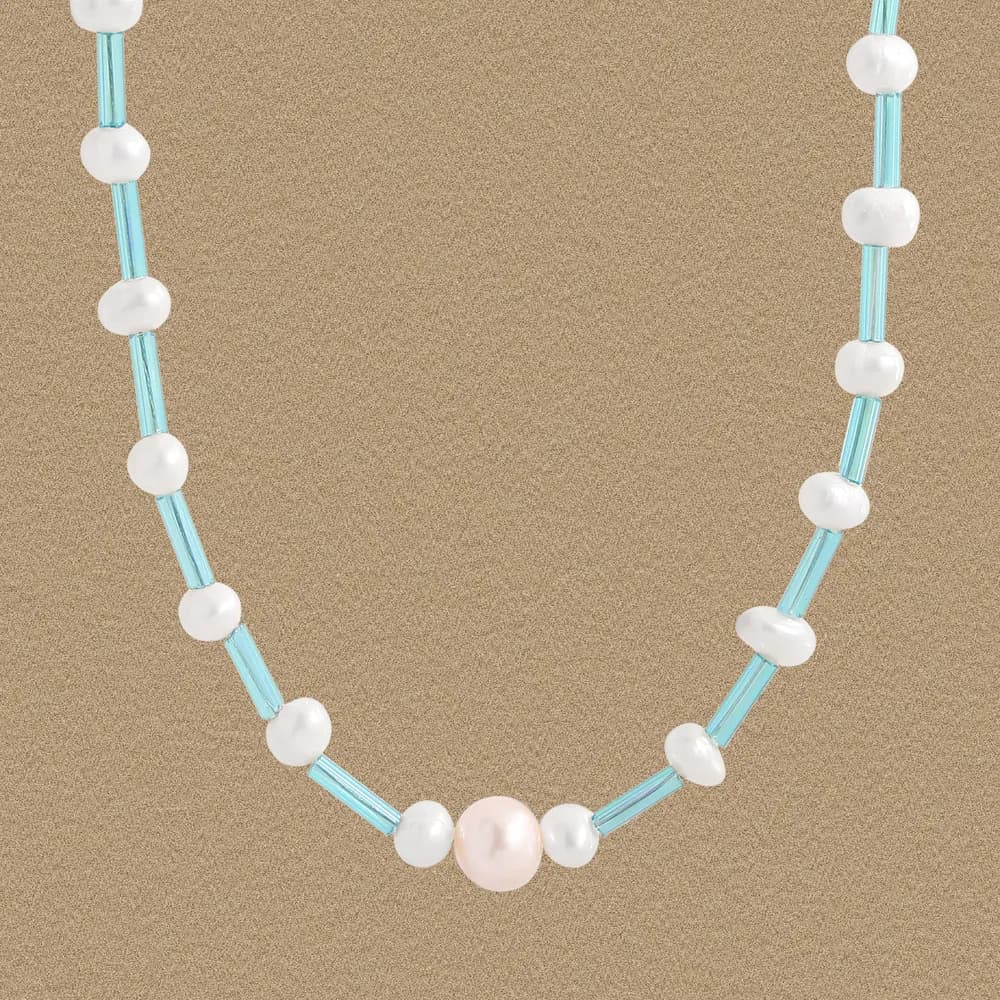 A close-up of a pearl and turquoise bead necklace resting on a neutral background.