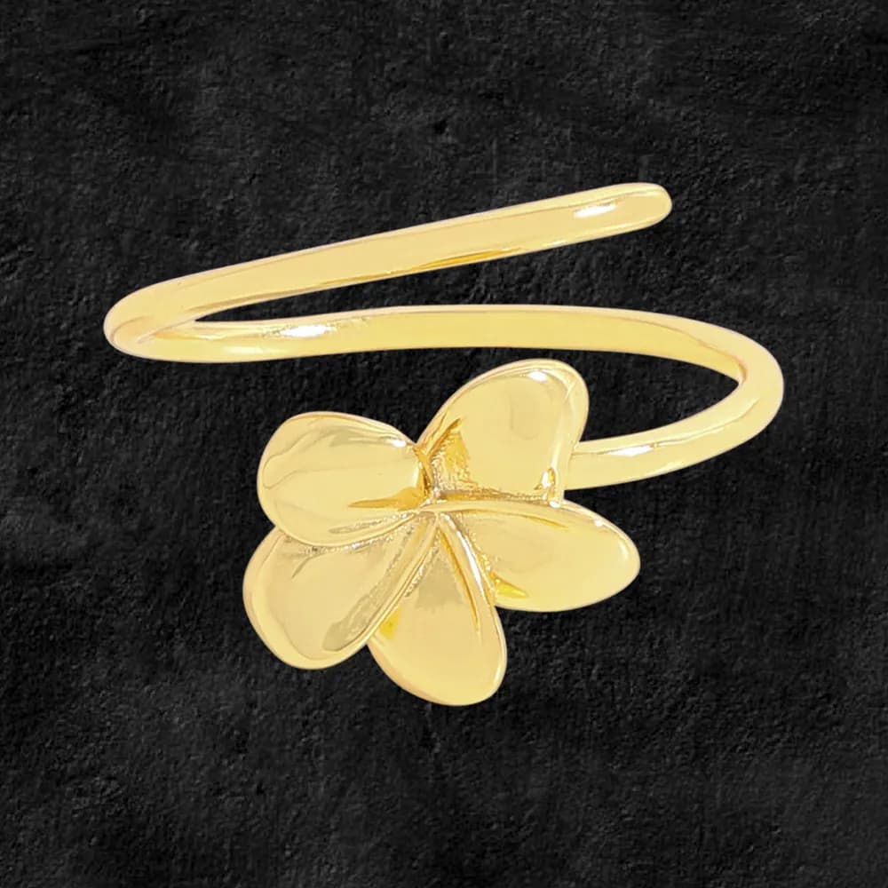Polished gold-tone clover ring with an open wrap band and four rounded petals on a dark background.