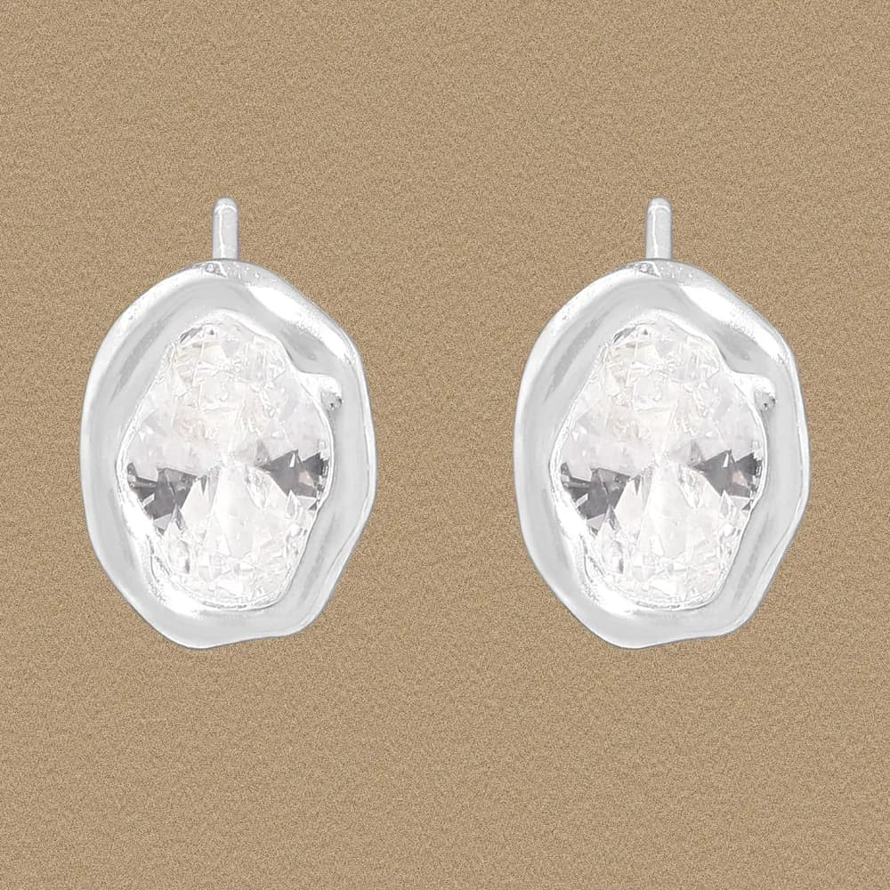 Pair of polished sterling silver earrings with irregular oval crystal gems set in bezels on a warm background.