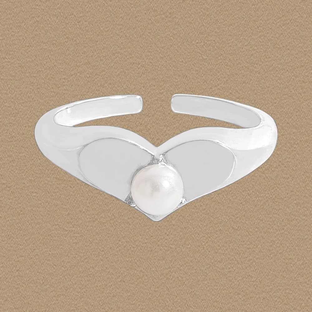 Open-ended sterling silver ring with a heart-shaped motif and a central pearl on a warm brown background.