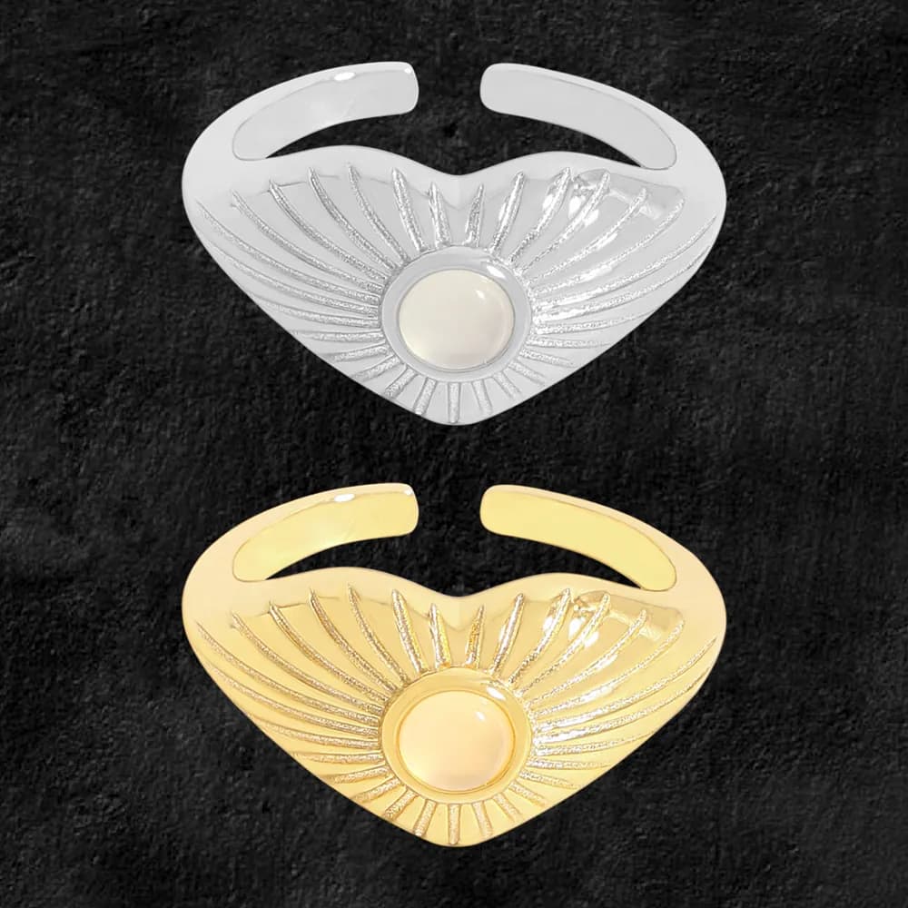 Open-heart ring with sunburst radiating lines and a central round cabochon, shown in silver and gold-tone finishes.