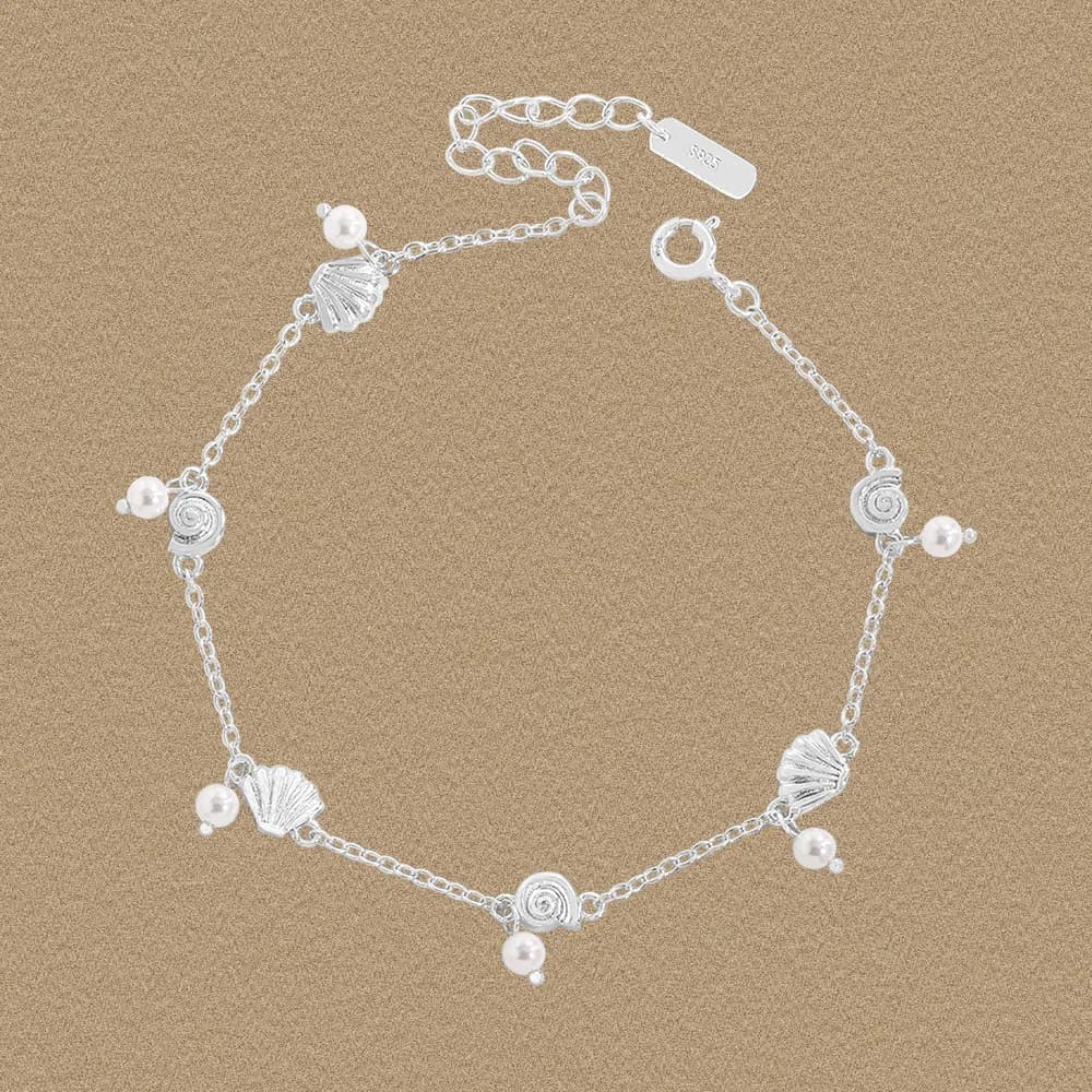 Sterling silver shell and pearl charm bracelet laid on a warm background with an adjustable clasp