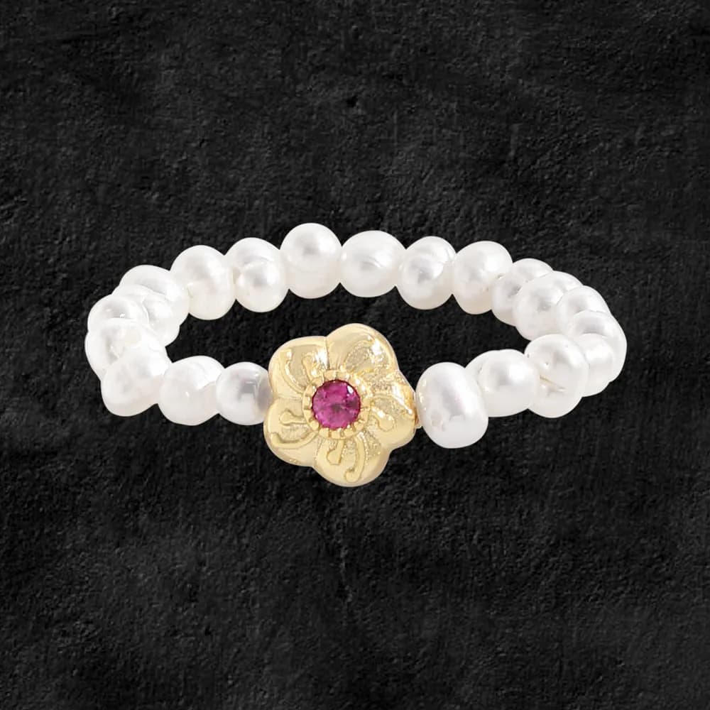 Close-up of a pearl bead ring with a gold-tone flower centerpiece featuring a pink gemstone.