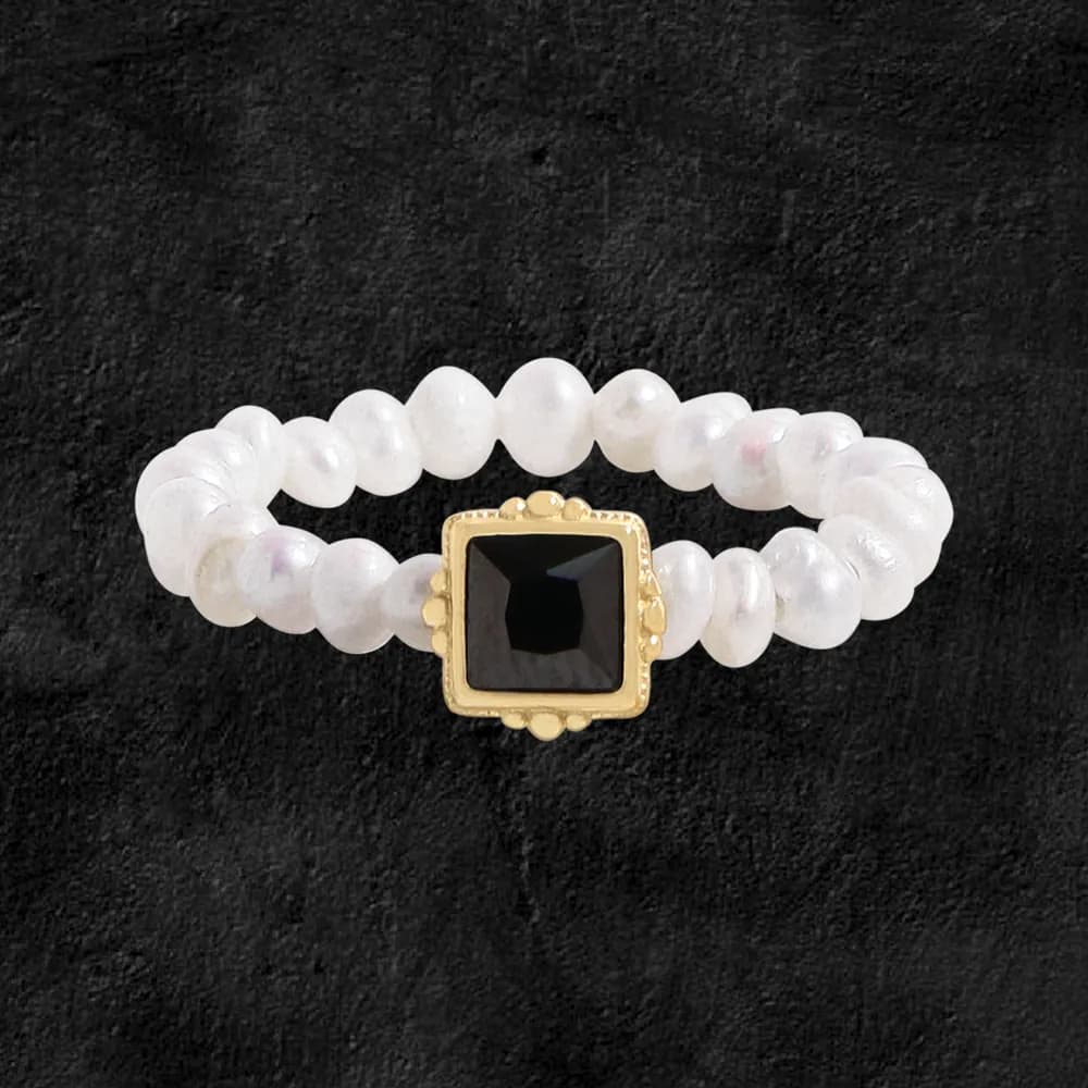 Close-up of a beaded sterling silver ring with a square black stone in a gold-toned bezel