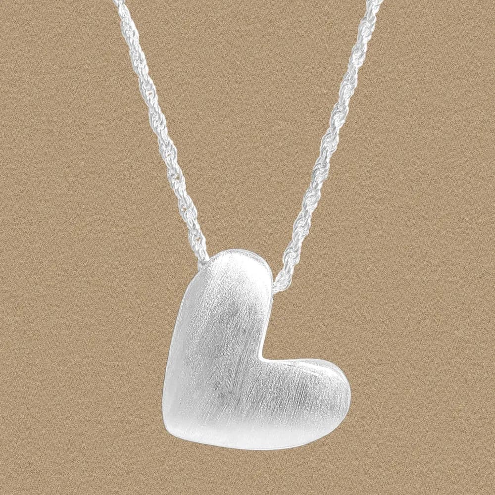 Sterling silver heart pendant on a twisted rope necklace, displayed against a warm beige background.