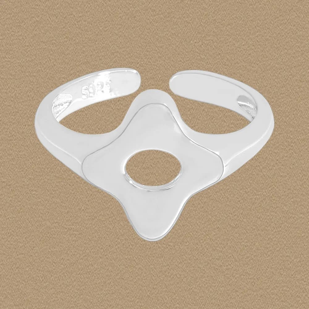 Polished sterling silver ring with a four-lobed top and central circular cutout on a sandy background.