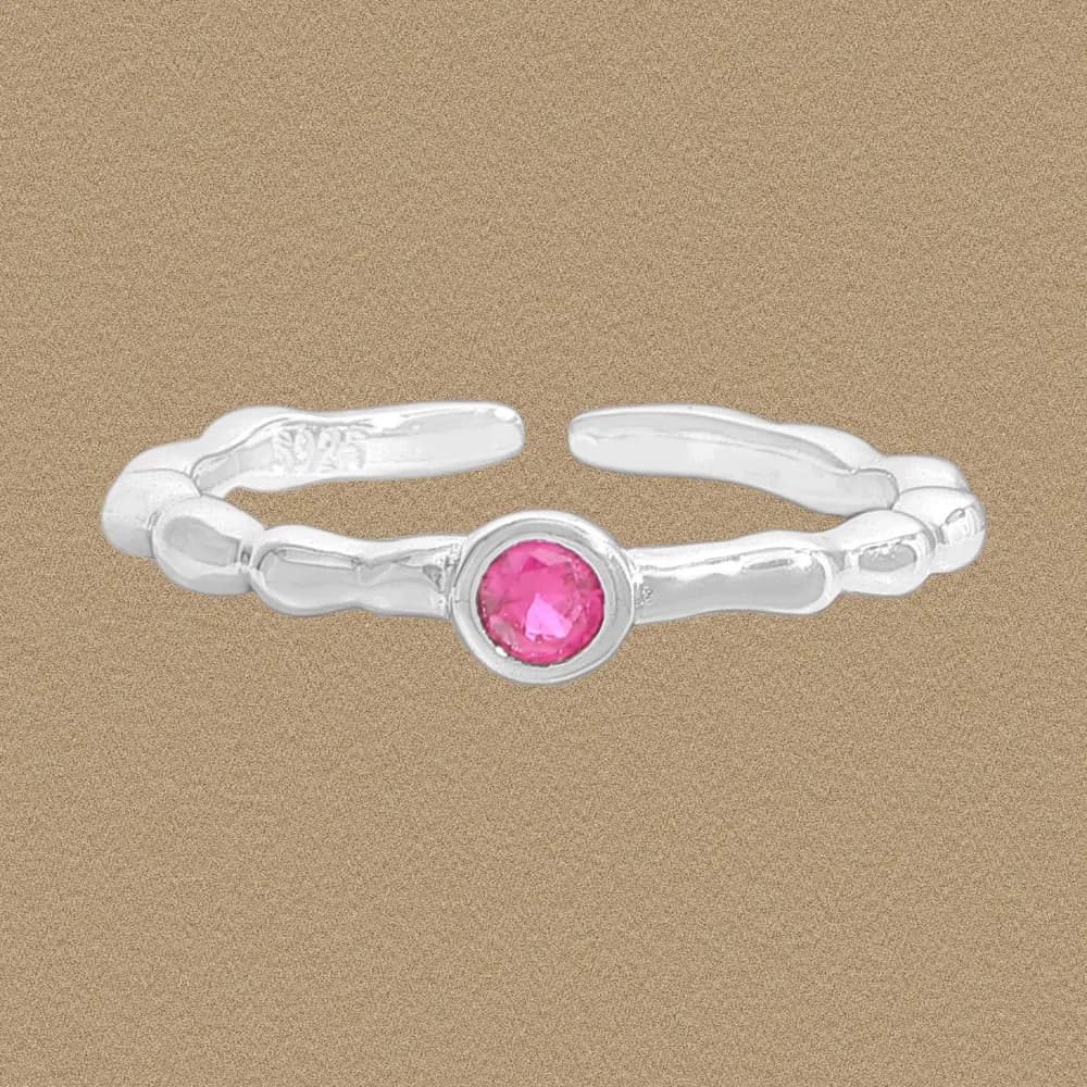 Open-ended sterling silver ring with a round pink gemstone in a bezel setting on a sandy background.