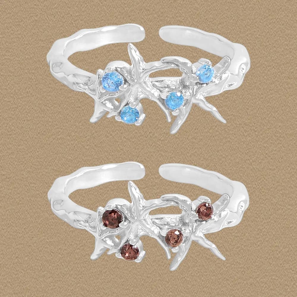 Two polished sterling silver coral-branch rings with blue and brown stones against a sandy background.