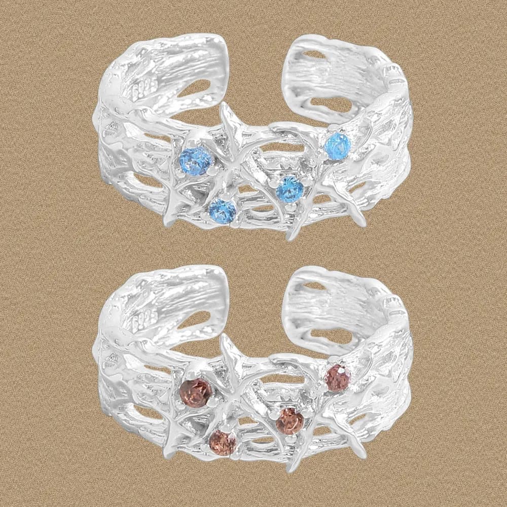 Two polished Sterling silver openwork rings with star motifs and blue stones on a sandy background.