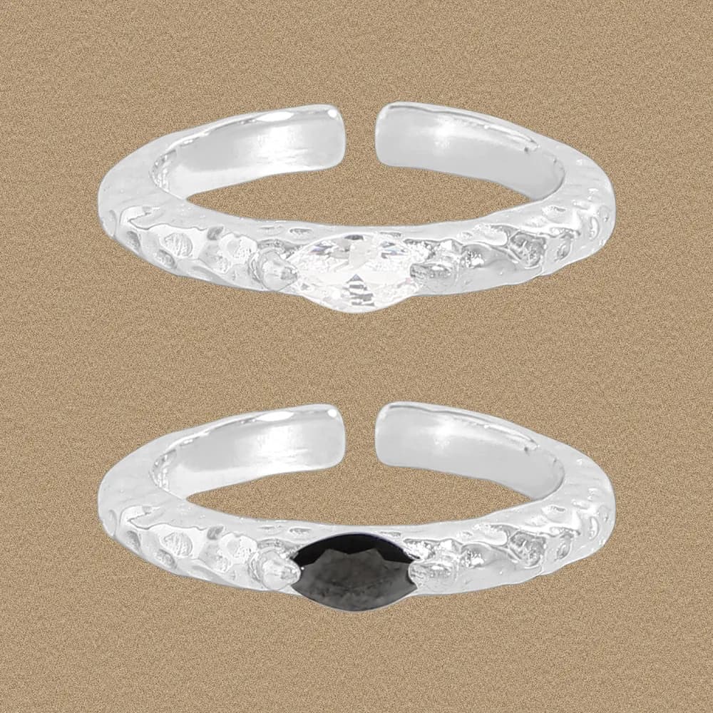 Two hammered sterling silver rings, one with a dark marquise centerpiece, resting on a sandy background.