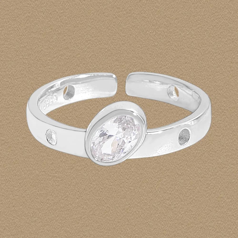 Polished sterling silver ring with an oval bezel-set clear stone and decorative circular cutouts on the band