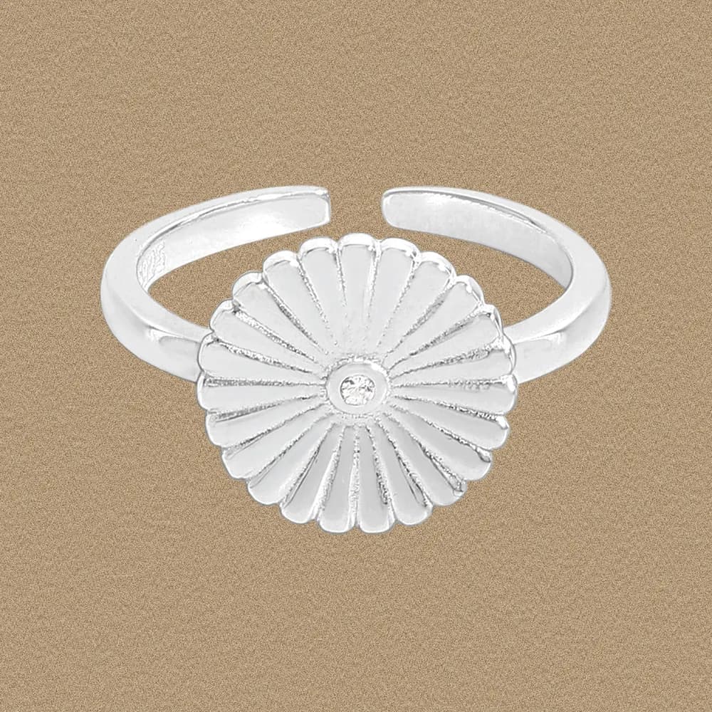 Polished sterling silver ring with a radiating daisy flower centerpiece and a tiny central gemstone on an neutral backdrop.