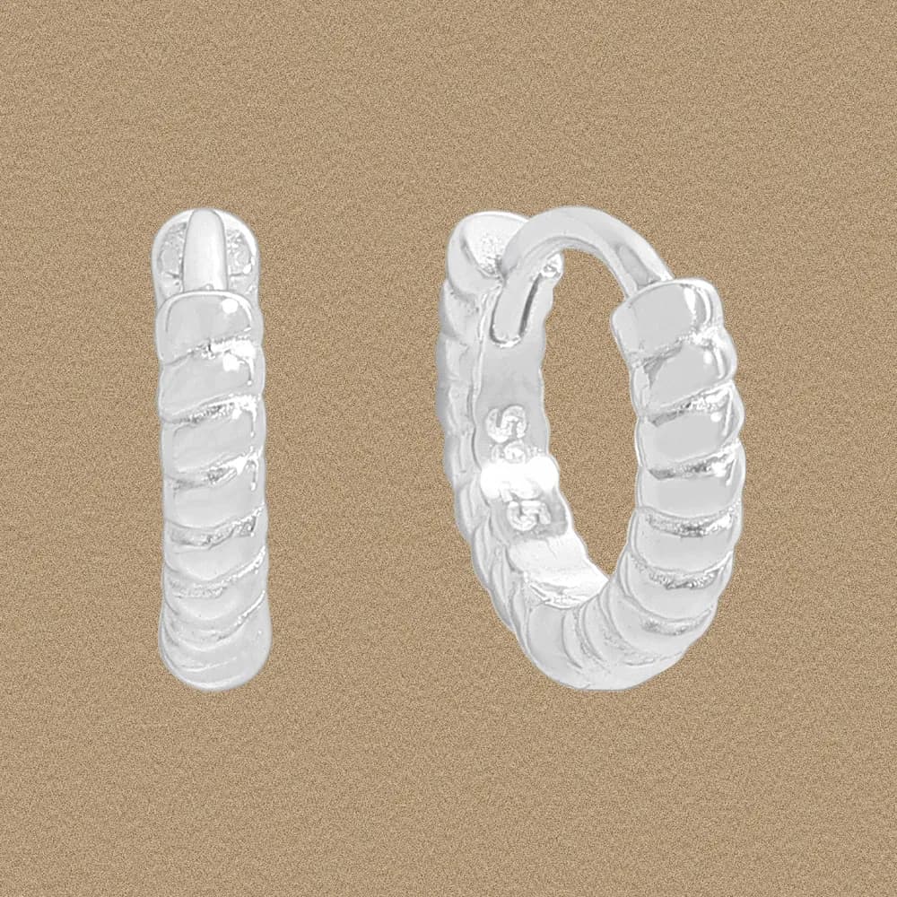 Polished sterling silver ribbed hoop earrings photographed against a warm beige background.