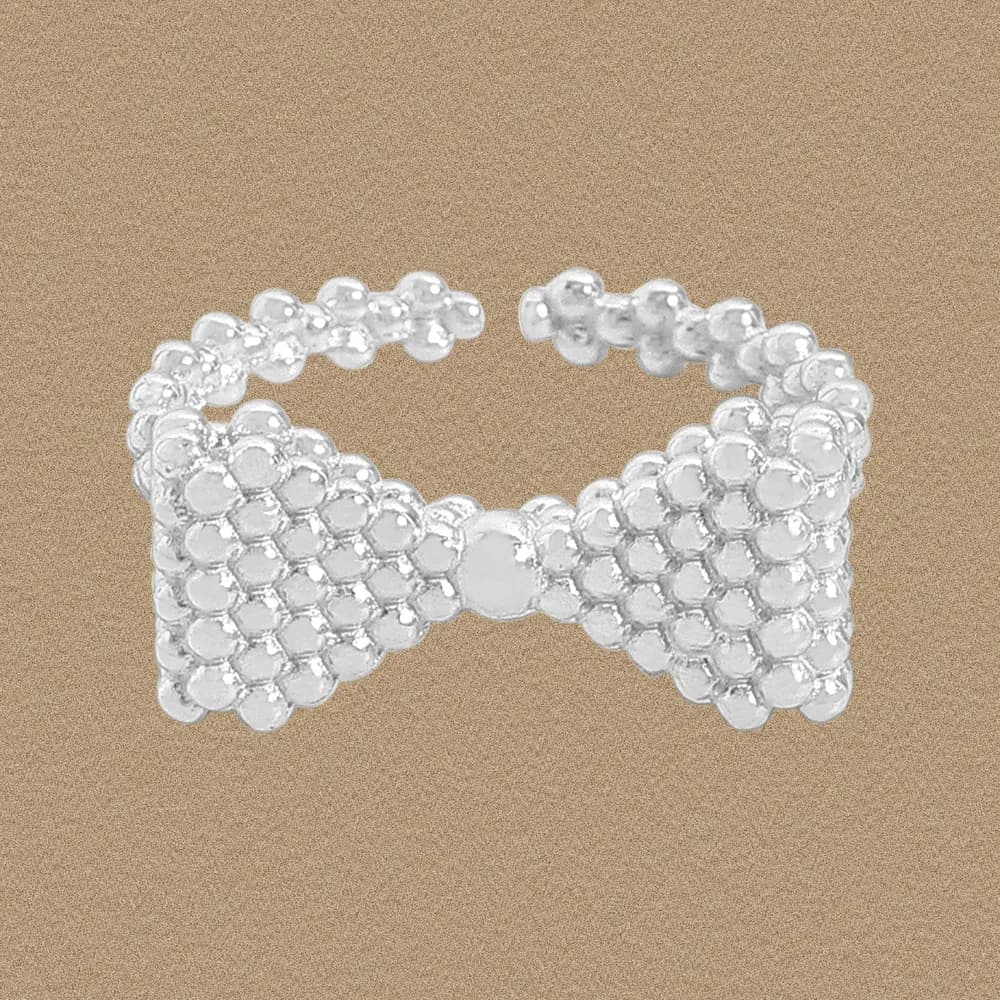 Polished sterling silver beaded bow ring resting on a warm, sandy background.