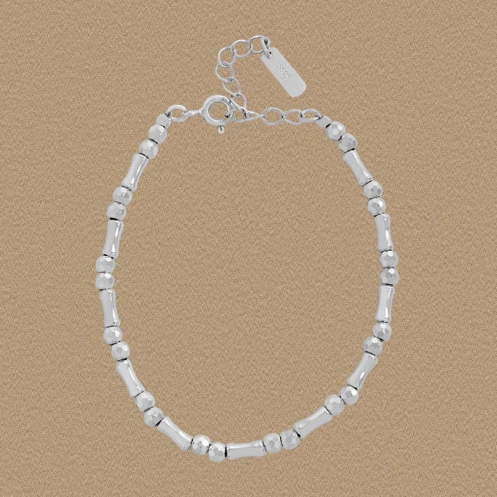 Polished sterling silver bracelet with alternating bead and barrel links laid on a light background.
