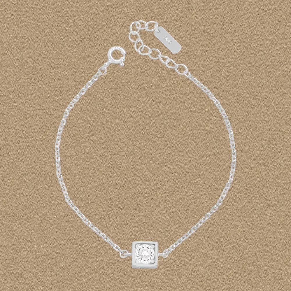 Sterling silver bracelet with a square bezel setting and a delicate chain on a textured background.