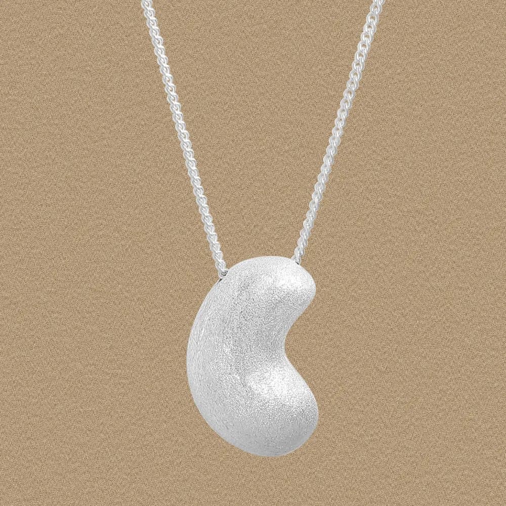 Close-up of a silver bean-shaped pendant on a delicate chain against a neutral background.