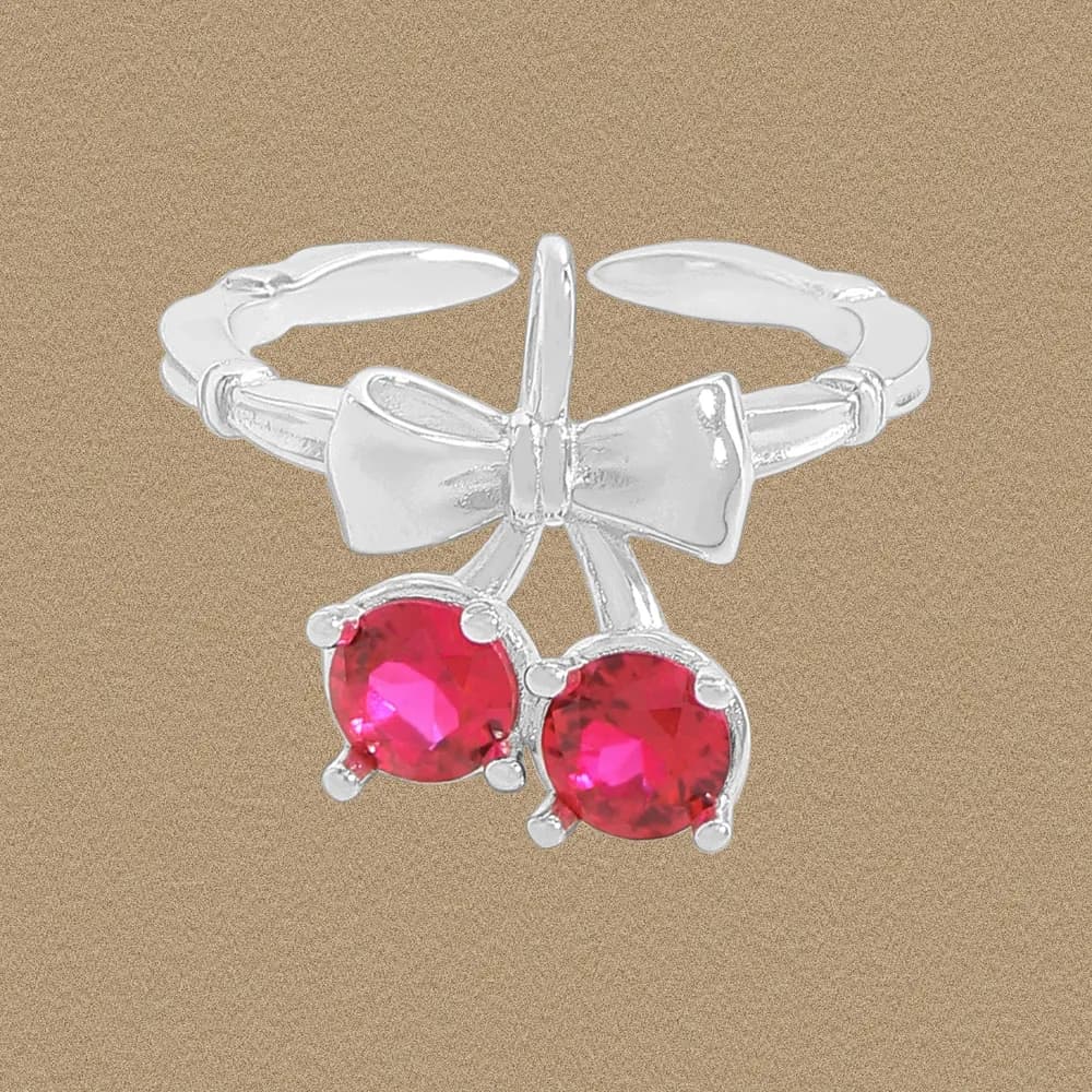 Polished sterling silver bow ring with two red gemstone drops hanging beneath.