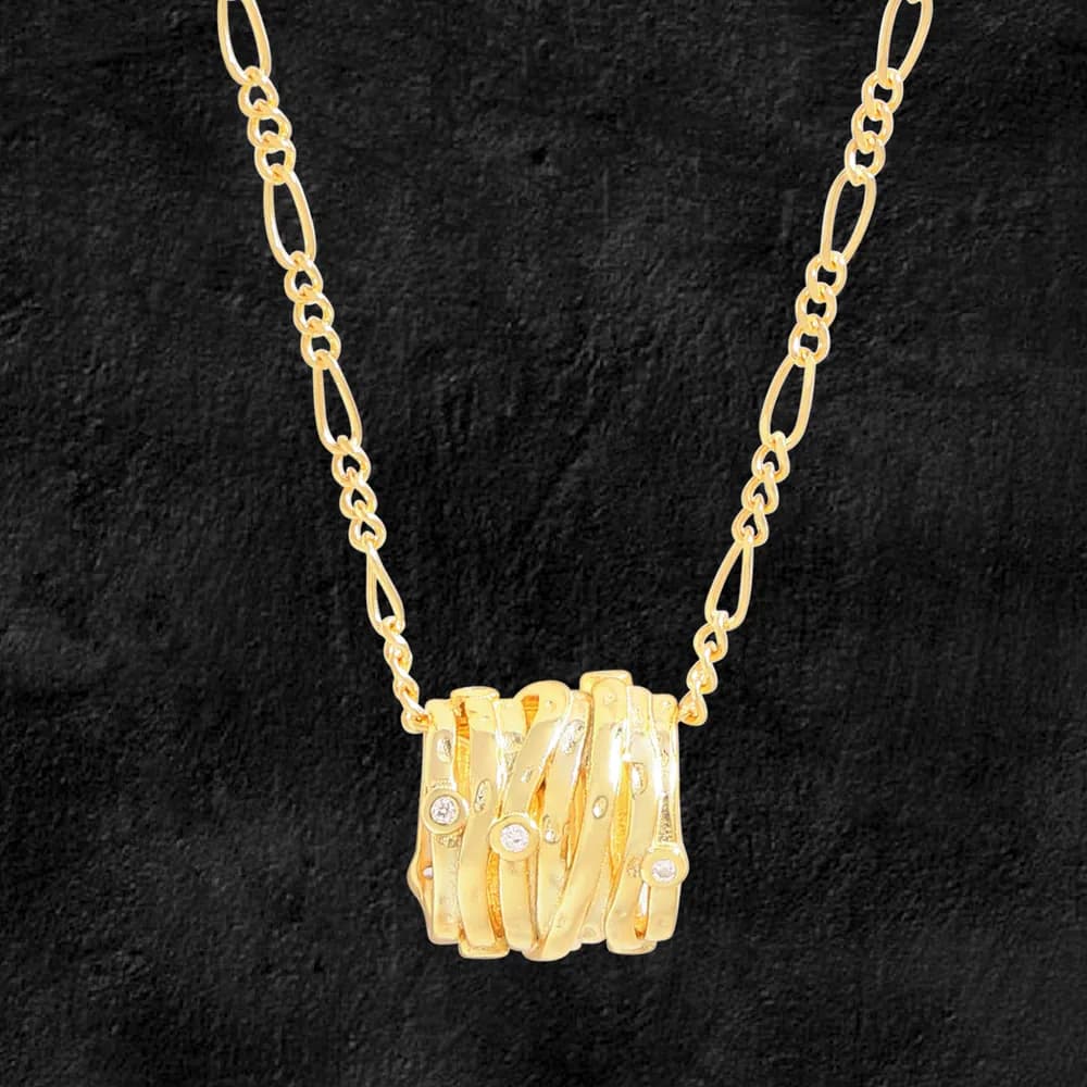 Polished gold-toned layered pendant necklace with intertwined bands and small stones on a chain against a dark background.
