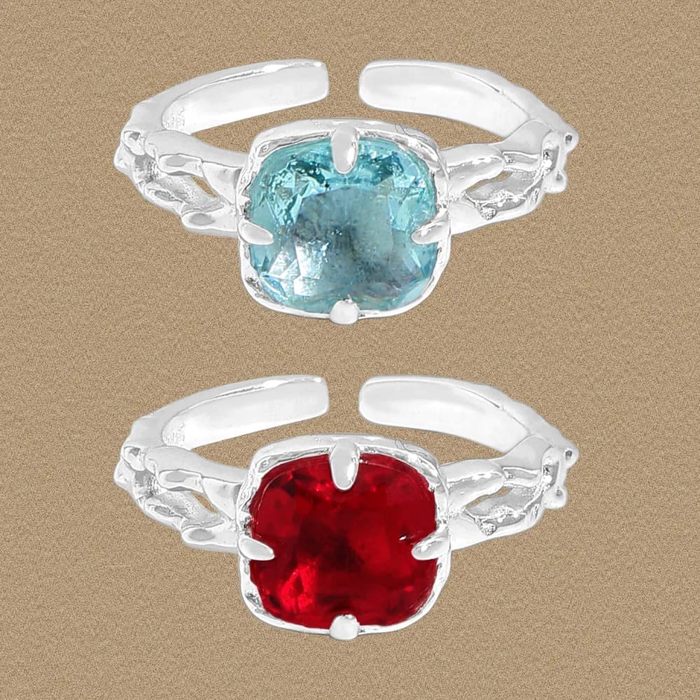 Two sterling silver rings with cushion-cut blue and red stones held by prongs