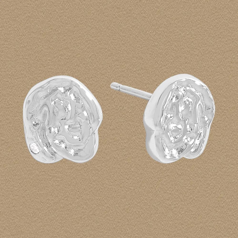 Close-up of polished sterling silver disk studs with irregular, hammered texture on a warm background.