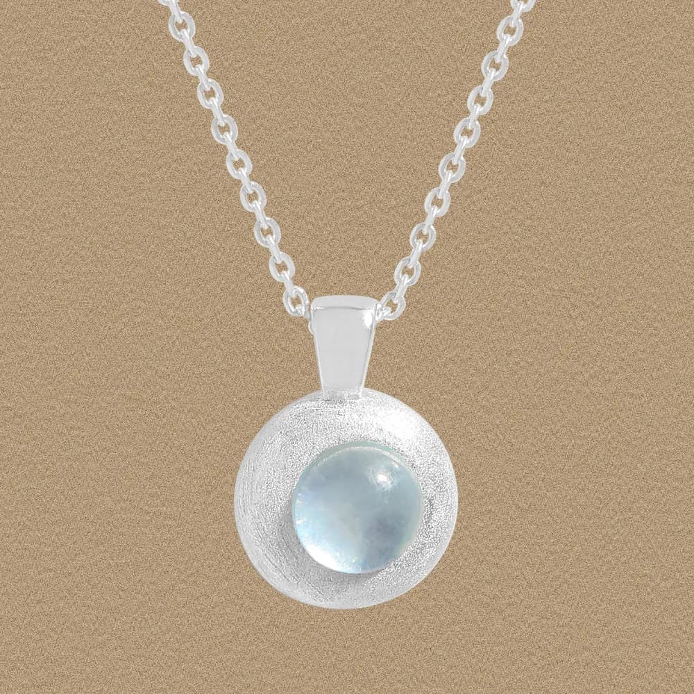 Sterling silver moonstone disc pendant on a chain against a warm beige background.