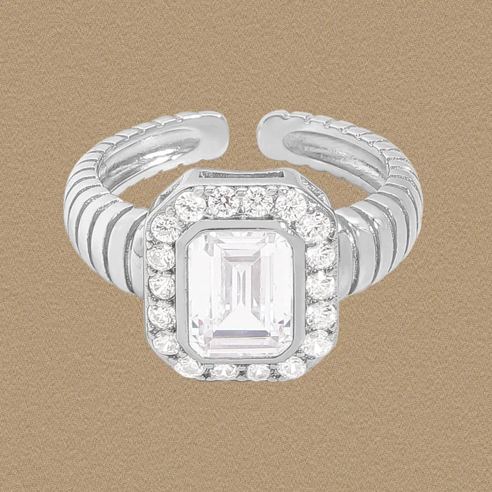 Silver ring with an emerald-cut center stone surrounded by a halo of small diamonds on a ribbed, adjustable band.