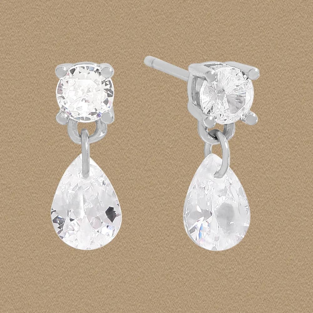 Close-up of two sterling silver drop earrings with round stud and teardrop crystal dangles