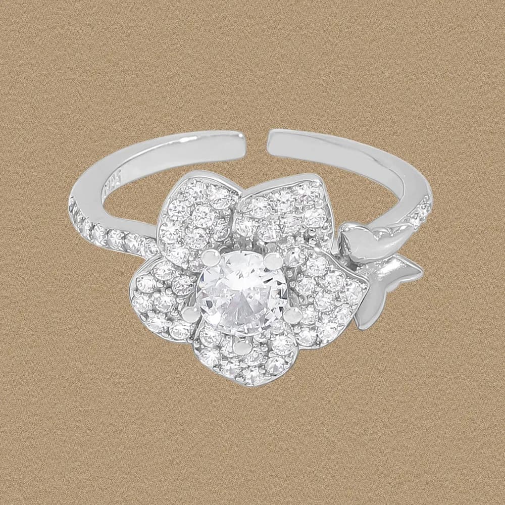 Polished sterling silver flower ring with a central clear stone and pavé petals against a warm background.
