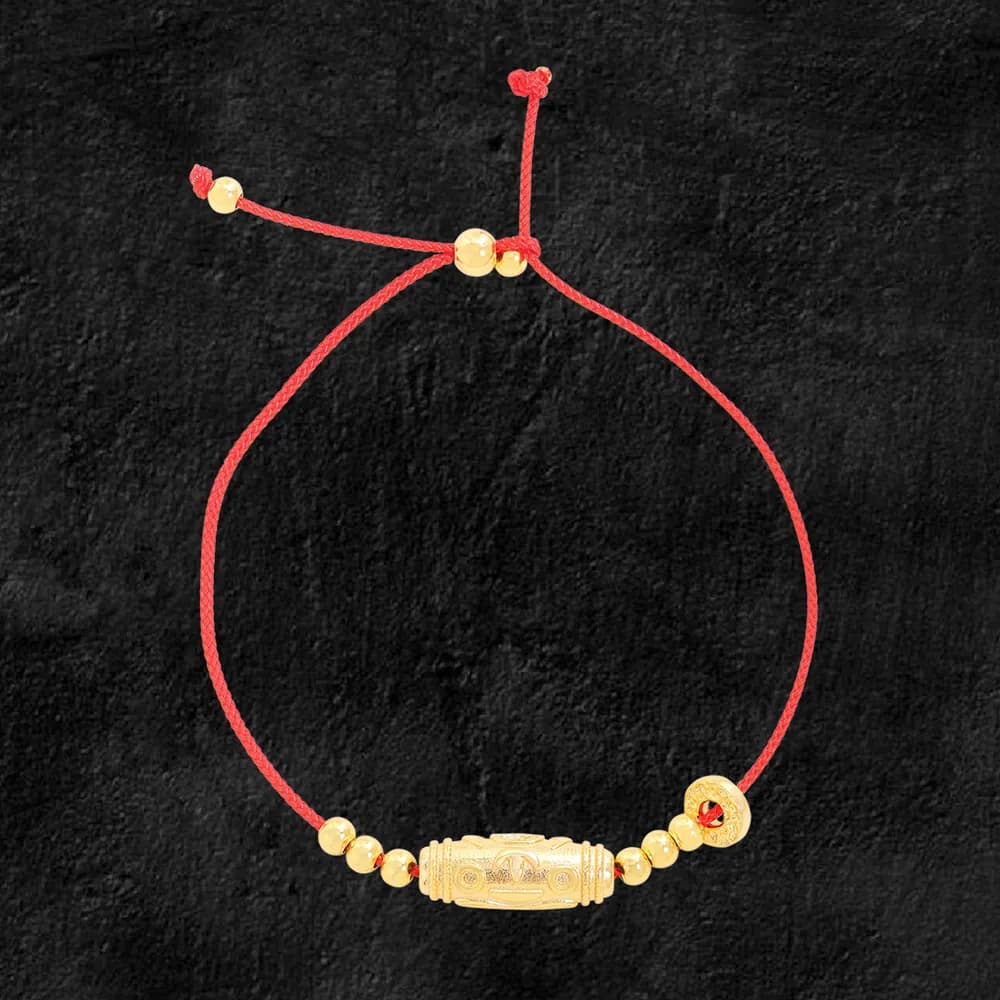 Red cord bracelet with a gold-toned cylindrical bead centerpiece and small beads on either side set against a dark background.