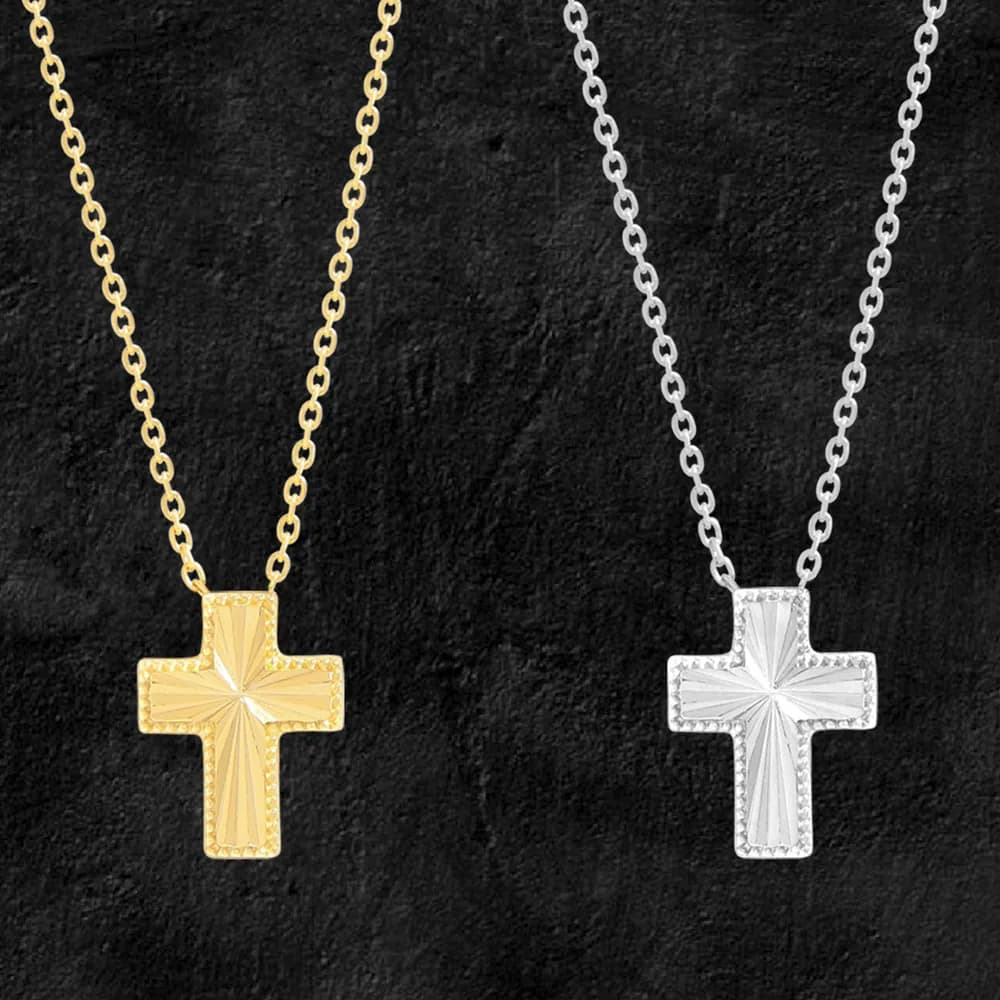 Two-tone cross pendant necklaces in gold-tone and silver-tone finishes on delicate chains against a dark background.